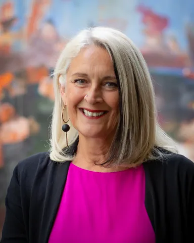A woman in pink and black top in front of a colorful background