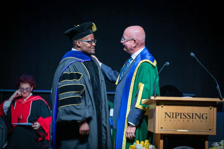 Dr. Jonathan Muterera receiving his award from Dr. Paul Cook on stage