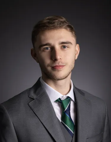 Hayden Lloyd smiles at the camera dressed in a grey suit.