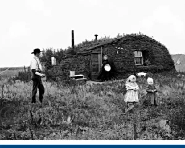 A black and white picture of a farmer family standing near their house in the fields