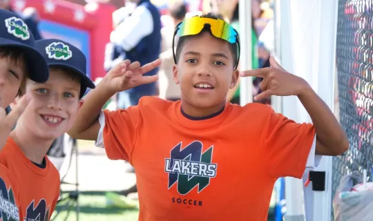Young boys posing in orange shirts that read "NU Lakers Soccer" during NU Homecoming 2025