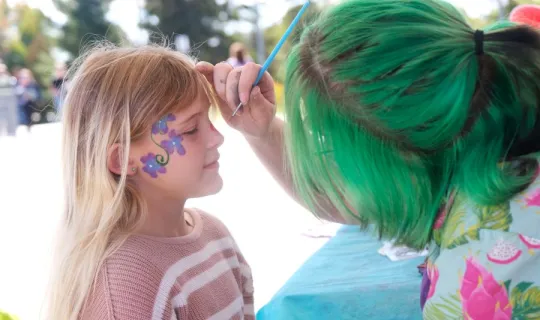 Young girl is getting a face painting during NU Homecoming 2025
