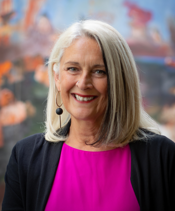 A woman in pink and black top in front of a colorful background