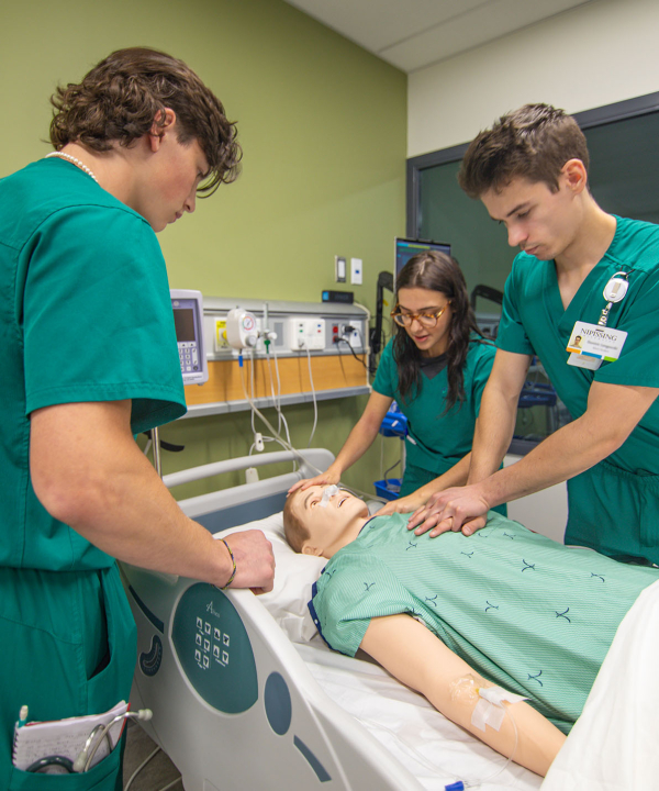 3 students in green scrubs doing chest compression on a mannequin in the simulation lab at Nipissing
