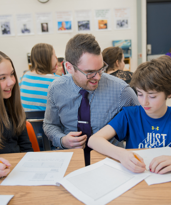 A teacher helping 2 students at a desk