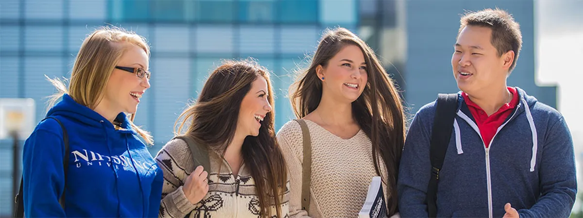 four students talking with the campus library in the background