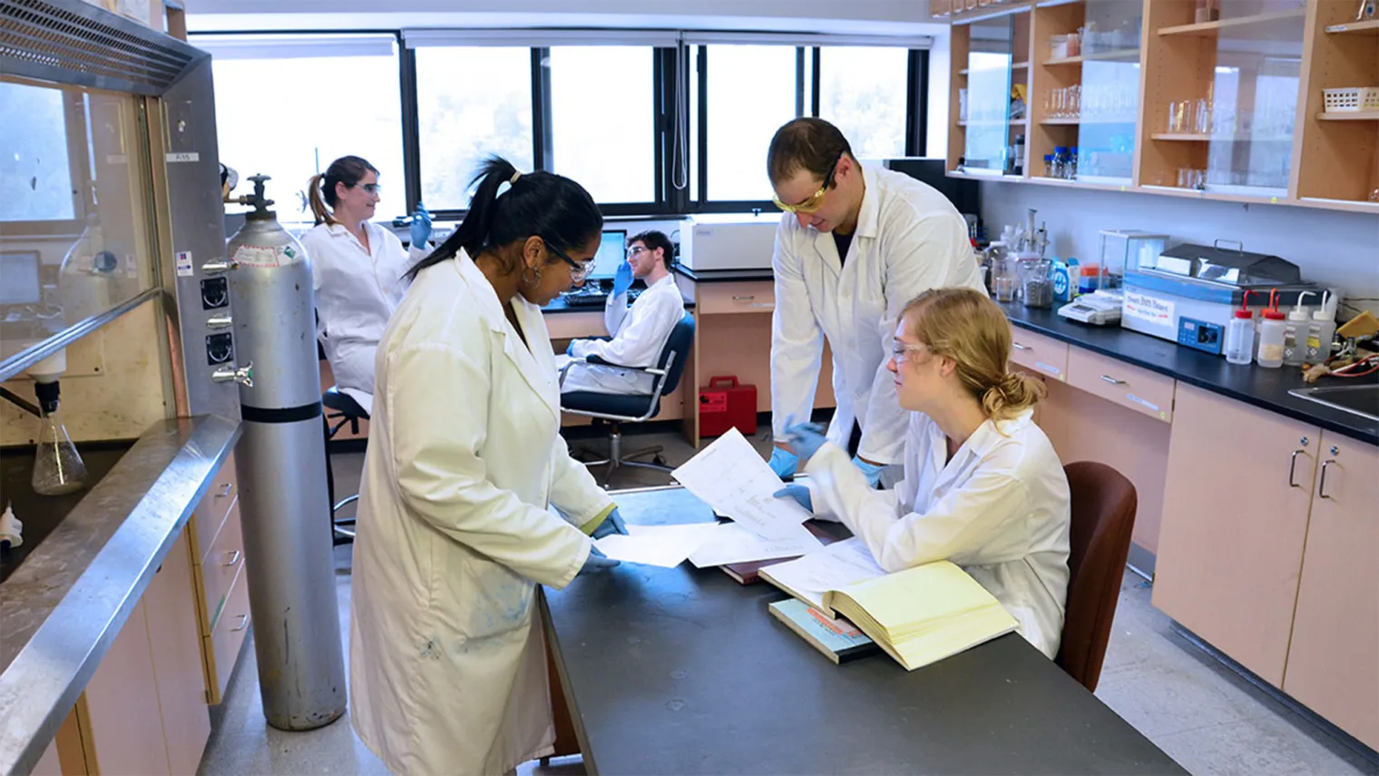3 students in lab coats working on an island in the middle of the science lab
